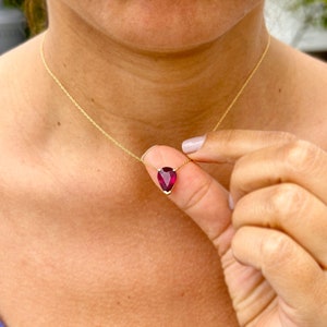 May include: A gold chain necklace with a teardrop-shaped, deep red gemstone pendant.