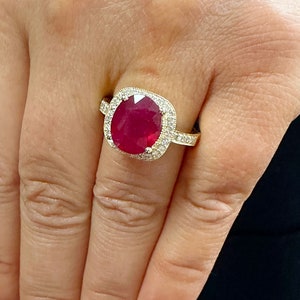 May include: A gold ring with a large oval ruby surrounded by a halo of smaller diamonds.