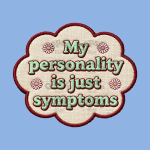 May include: An embroidered patch with the phrase "My personality is just symptoms" in mint green lettering. The patch has a cream-coloured background, a scalloped edge, and is outlined in dark red. Small daisy accents are placed around the text.