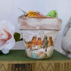 May include: A whitewashed terracotta flower pot with a vintage bird and egg design. The pot is decorated with the words "Paris" and "Paffard".