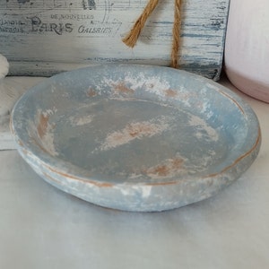 May include: A small, round, distressed-finish bowl. The bowl is painted a light blue with white and tan accents. The rim has a tan edge. The bowl is likely made of wood or a similar material. Decorative home decor.