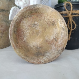 May include: A round, beige ceramic planter with a distressed finish. The planter has a rough, textured surface with a light brown and white color scheme.