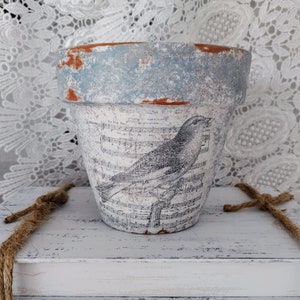 May include: A blue and white terracotta planter with a distressed finish features a black and white image of a bird singing on a branch with musical notes in the background.