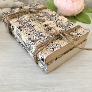 May include: Two books stacked on top of each other, wrapped in brown twine and decorated with a black and white patterned paper. The paper features a floral design and a small bee.