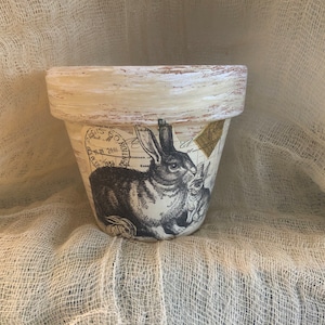 May include: A white ceramic planter with a distressed finish features a black and white image of a rabbit with a vintage stamp design.