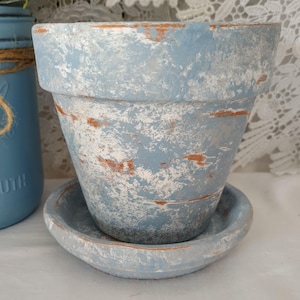May include: A blue terracotta planter with a distressed white and brown paint finish. The planter has a matching saucer.