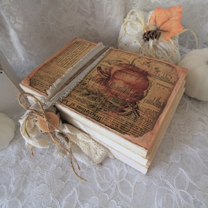 May include: A stack of vintage-style books with a brown paper cover and a decorative image of a pumpkin on the top book. The books are tied together with twine and lace.