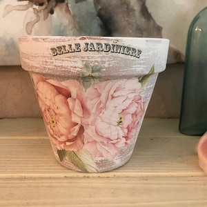 May include: A white ceramic planter with a distressed finish and a floral design. The planter has the words "Belle Jardiniere" written on it.