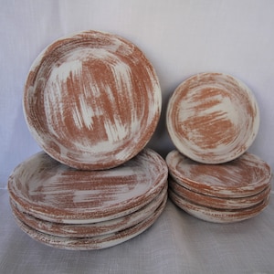 May include: Set of six terracotta plates with a white glaze. The plates are stacked in two piles, one with three plates and one with two plates. The plates have a rustic, handmade look.