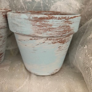 May include: A light blue terracotta planter with a distressed finish. The planter has a rustic look with brown showing through the blue paint.