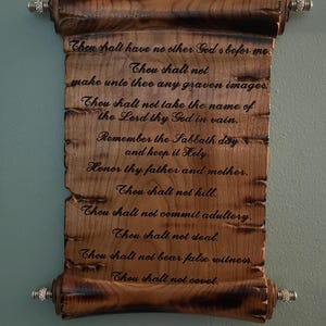 May include: A wooden scroll with the Ten Commandments inscribed in black lettering. The scroll is made of dark brown wood with decorative silver-colored end pieces. The text is clearly visible.
