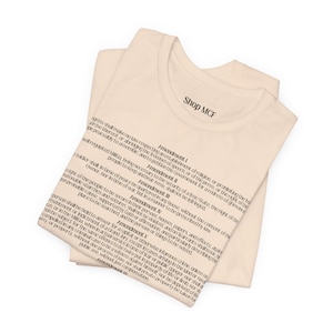 May include: Off-white t-shirts with the text of the first five amendments of the U.S. Constitution printed in black. The shirts are folded, with the words "Shop MCF" printed on the top shirt.