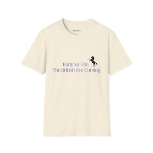 May include: Cream-colored t-shirt with the text "Body So Tea The British Are Coming" in purple and a black horse silhouette. The shirt also has the text "Shop MCF" at the top.