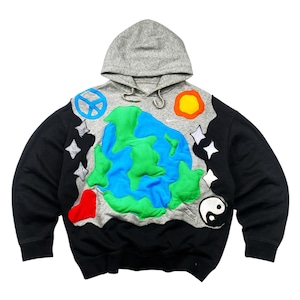 Op de afbeelding: Een zwarte en grijze hoodie met een kleurrijk applicatieontwerp. Het ontwerp omvat een blauwe en groene aarde, een vredesteken, sterren, een hart, een yin-yang symbool en een zon. De capuchon is grijs.