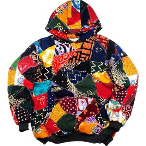 May include: A patchwork hoodie with a vibrant mix of colors and patterns. The hoodie features a kangaroo pocket, a drawstring hood, and black ribbed cuffs and hem. The design incorporates various fabric pieces in red, yellow, blue, and green.