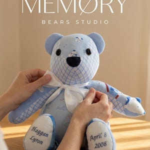 May include: A blue and white memory bear with a bow tie, personalized with the name "Haggan Lyron" and the date "April 8 2008". The bear is handcrafted and weighted to match birth weight. The text "MEMORY BEARS STUDIO" is visible.