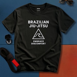 May include: Black t-shirt with white text reading "BRAZILIAN JIU-JITSU" above a triangle and wave graphic, with the words "EMBRACE DISCOMFORT". A black belt with a red stripe, a mouthguard, and tortoiseshell sunglasses are also visible.
