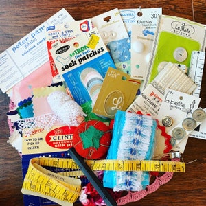 May include: A collection of vintage sewing supplies, including buttons, lace, ribbon, thread, and fabric scraps. The items are arranged on a wooden surface and include a variety of colours and patterns.