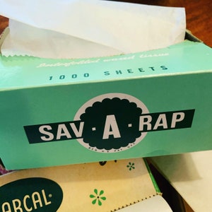May include: A green box with the text "Interfolded waxed tissue 1000 sheets" and a green circle with the text "SAV-A-RAP" in white letters. The box is partially open and there is a white tissue paper inside.
