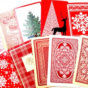 May include: A collection of playing cards featuring various red and white designs, including a decorated Christmas tree, a black silhouette of a deer, snowflakes, plaid patterns with the monogram MMD, and intricate floral and geometric borders.