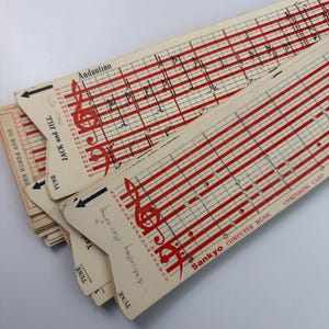 May include: A stack of off-white Sankyo Computer Music composing cards featuring red musical staves, treble clefs, and printed text including "Jack and Jill" and "Do not punch here." The cards have pre-punched holes for mechanical music boxes.