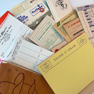 Op de afbeelding: Een verzameling vintage papieren documenten en briefpapier, waaronder een geel bedankje notitieblok, een bridge scorekaart, een Gulfgas LP-Gas bon en een Southwest Land Title Co. document. De documenten liggen verspreid op een wit oppervlak.