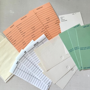 May include: A selection of vintage library cards in various colours. Includes orange "RESERVED" cards, green "DATE DUE" cards, and white cards with "DATE" and lined sections. Some cards have text like "3976.3 LEV LeVert Louisiana cop. 1".