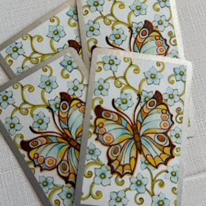 May include: A set of rectangular playing cards featuring a repeating pattern of light blue five-petaled flowers with yellow centers and green vines. Each card displays a large butterfly with blue, yellow, and brown wings in the center.