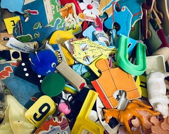 May include: A colorful assortment of wooden puzzle pieces, including a blue and green piece shaped like a horseshoe, a yellow piece shaped like a letter 'U', and a red piece with the text 'PACIFIC OCEAN'.