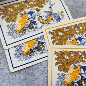 Op de afbeelding: Drie geïllustreerde kaarten met een blauw en geel kleurenschema. Elke kaart toont een ander dier, waaronder een hert, een vos en een beer. De kaarten zijn omringd door een verscheidenheid aan andere dieren en planten.