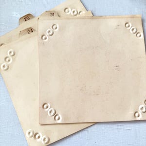 May include: A stack of vintage index cards in a light tan color. Each card has a series of embossed circles in the corners. Some cards have small tabs with numbers 24, 25, and 31.