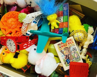 May include: A box filled with a variety of colorful toys, including a blue airplane, a white bunny, a yellow troll doll, a red and white sun, and a book titled "The Boyhood of Wild Bill".