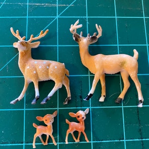 May include: Four plastic toy deer figurines. Two are larger and have brown and white spotted bodies with antlers. Two are smaller and are solid brown with no antlers.