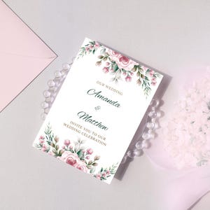May include: A white wedding invitation with a floral design featuring pink roses and green leaves. The text reads "Our Wedding Amanda & Matthew Invite you to our Wedding Celebration."