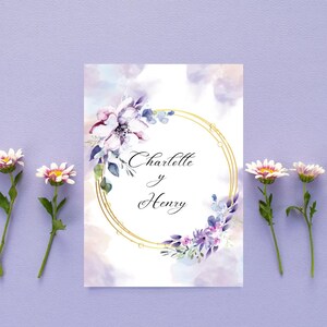 K&ouml;nnte beinhalten: Eine Hochzeitseinladung mit einem goldenen, kreisf&ouml;rmigen Rahmen und floralen Akzenten in Lila und Wei&szlig;. Die Namen "Charlotte y Henry" sind in den Rahmen geschrieben, vor einem Aquarellhintergrund.