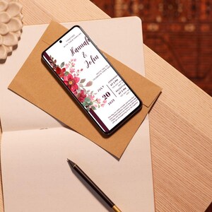 K&ouml;nnte beinhalten: Ein Smartphone zeigt eine Hochzeitseinladung mit den Namen "Hannah & John" und Veranstaltungsdetails. Die Einladung hat rote und rosa Blumendekorationen. Das Telefon liegt auf einem braunen Umschlag, auf einem Notizbuch, mit einem Stift daneben.