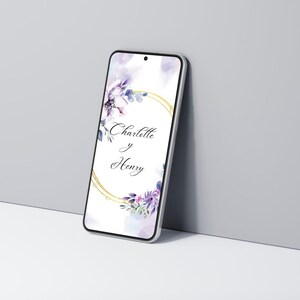 K&ouml;nnte beinhalten: Ein Smartphone zeigt ein Hochzeitskarten-Design. Der Bildschirm zeigt die Namen "Charlotte y Henry" in einem goldenen kreisf&ouml;rmigen Rahmen, umgeben von Aquarell-Blumenelementen in Lila- und Blaut&ouml;nen.