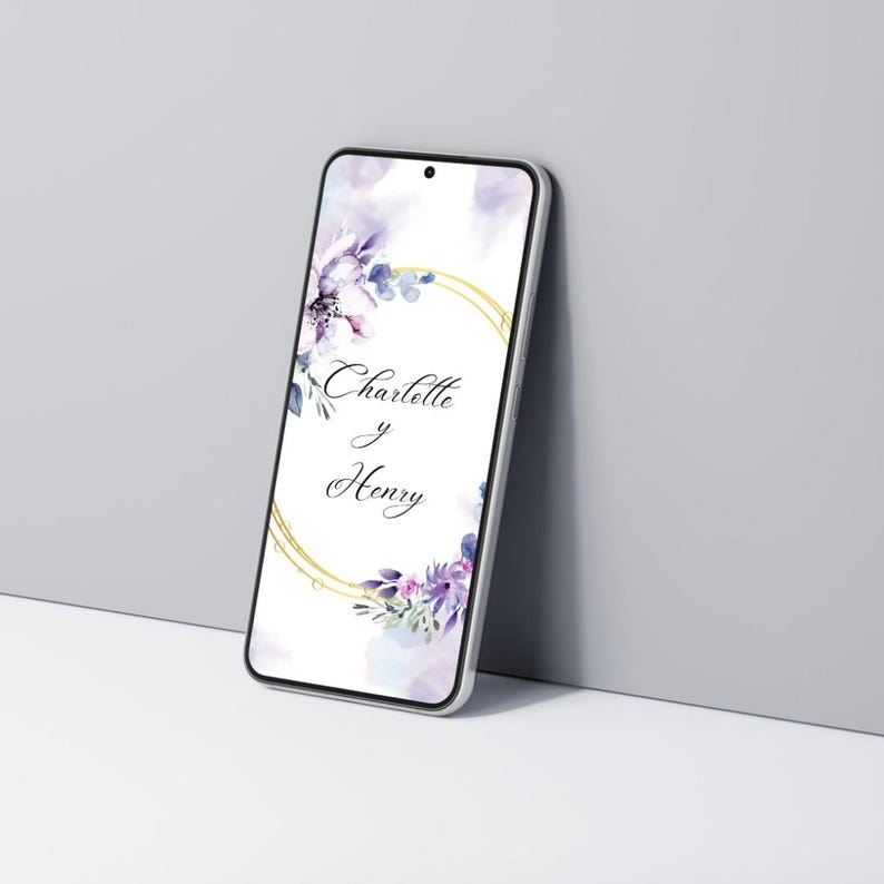 K&ouml;nnte beinhalten: Ein Smartphone zeigt ein Hochzeitskarten-Design. Der Bildschirm zeigt die Namen "Charlotte y Henry" in einem goldenen kreisf&ouml;rmigen Rahmen, umgeben von Aquarell-Blumenelementen in Lila- und Blaut&ouml;nen.