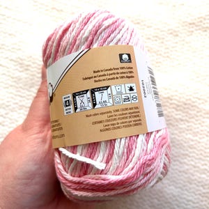 May include: A ball of pink and white variegated cotton yarn. The label indicates it's made in Canada and provides washing instructions. The yarn is suitable for medium-weight projects, with measurements of 4.5mm and 5mm.