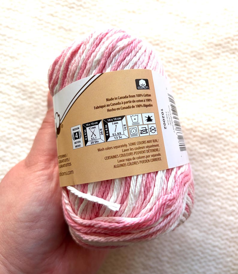 May include: A ball of pink and white variegated cotton yarn. The label indicates it's made in Canada and provides washing instructions. The yarn is suitable for medium-weight projects, with measurements of 4.5mm and 5mm.