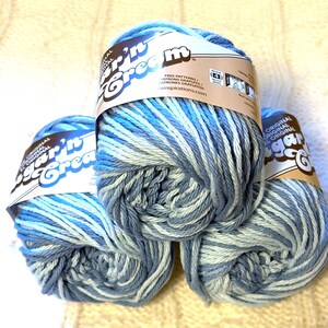 May include: Three skeins of Sugar'n Cream yarn in shades of blue and white. The yarn is labeled with the brand name and information about free patterns. The yarn is suitable for knitting and crochet projects.