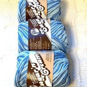 May include: Three skeins of blue variegated yarn, each with a brown label featuring the text "Sugar'n Cream". The yarn is a blend of light and dark blues, perfect for knitting or crocheting projects. The labels also include the text "The Original".
