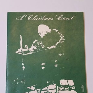 May include: A green program for a performance of A Christmas Carol at The Guthrie Theater. The program features a black and white silhouette of a man sitting at a table.