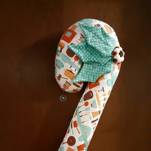 May include: A white candy cane pillow with a teal and white holly leaf design. The pillow is decorated with a variety of kitchen-themed patterns, including pots, pans, and utensils.