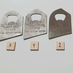 May include: Three silver bottle openers with the text "ORDER "VANITY FAIR" FLOUR FOR BETTER BREAD."  The openers are arranged in a row from left to right, labeled X, Y, and Z.