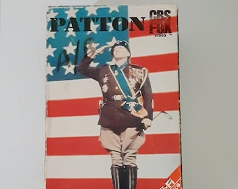 May include: VHS tape for the movie "Patton" featuring George C. Scott and Karl Malden. The cover displays a portrait of a saluting officer against a backdrop of the American flag. The tape is labeled "CBS Fox Video".