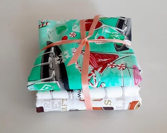 May include: A stack of two folded fabric pieces tied with a peach ribbon. The top fabric is teal with a pattern of red cocktails, peppermint candies, and snowflakes. The bottom fabric is white with a pattern of brown beer mugs and text.