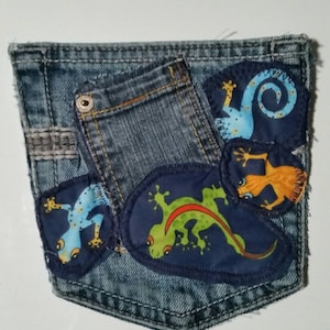 May include: A blue denim pocket with four colorful embroidered geckos. The geckos are in various poses and colors, including blue, green, orange, and yellow.
