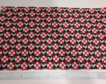 May include: A rectangular piece of fabric featuring a repeating pattern of black and white roosters set against a red, black, and white checkerboard background. A metal ruler is positioned along the bottom edge, showing a length of 22 inches.
