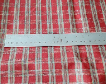 May include: A red fabric featuring a plaid pattern with thin white and light blue vertical and horizontal lines. A metal ruler is placed across the fabric, showing a measurement of approximately 8 inches in length across the visible section.